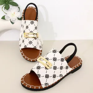 Gros plan de sandales plates pour femmes avec tige à motifs et boucle dorée élégante.