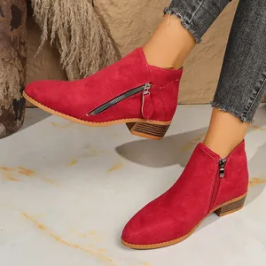 Detail shot of stylish red suede ankle boots with side zippers and low block heels