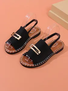 Détail rapproché de sandales plates noires avec boucle dorée et bride élastique