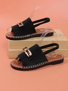 Détail de sandales plates noires pour femmes avec boucle en métal doré et élastique