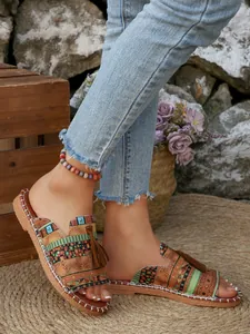 Nahaufnahme von flachen Damensandalen im Ethno-Stil mit Quasten und Stammesmustern.