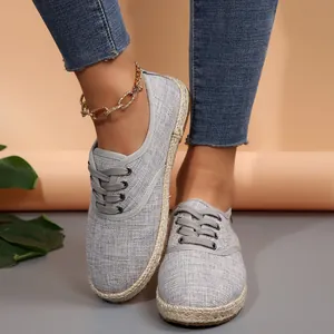 Detail van grijze canvas espadrilles met veters gedragen met blauwe jeans en enkelband.
