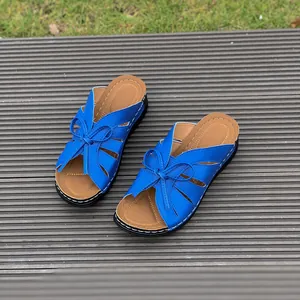 Blue women's wedge sandals with butterfly bow and cut-out details on a grey deck.