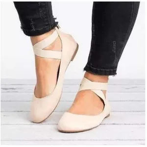 Close-up detail of beige retro flat shoes featuring elastic cross ankle straps on a model