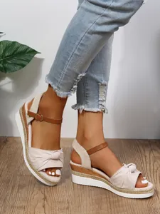 Vista laterale di sandali con zeppa beige con fiocco e suola in corda intrecciata.