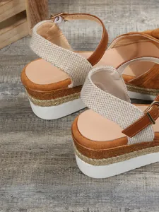 Primo piano di sandali marroni con zeppa, cinturini intrecciati e bordo oro.