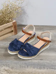 Sandali con zeppa blu navy con dettaglio nodo e plateau in corda su pavimento legno.