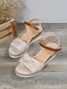 Dettaglio di sandali beige con zeppa, fiocco e suola in corda intrecciata.