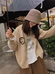 Woman wearing beige smiley face cardigan and brown bucket hat in outdoor street setting