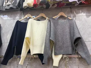 Dettaglio dei maglioni in maglia larghi con spalle scoperte in nero, crema e grigio