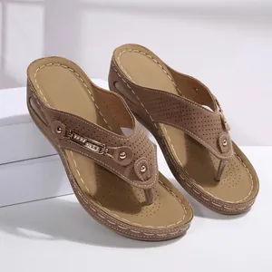 Detalle de sandalias con cuña marrones con pedrería y patrones cortados por láser.