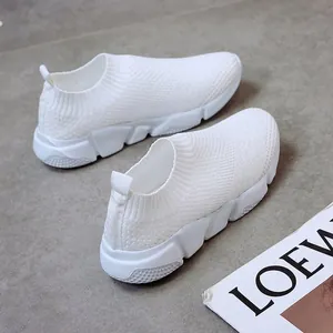 Close-up view of white breathable flyknit sneakers with thick soles on a textured grey floor