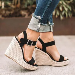 Dettaglio di sandali neri con zeppa e plateau indossati con jeans blu alla moda.