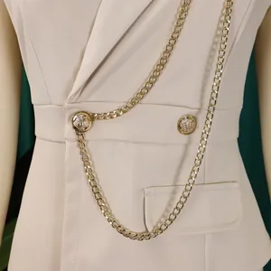Close-up detail of a beige blazer jumpsuit with ornate gold buttons and metal chain decor