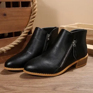 Close-up of black pointed-toe ankle boots featuring side zipper and chunky heel on wooden background