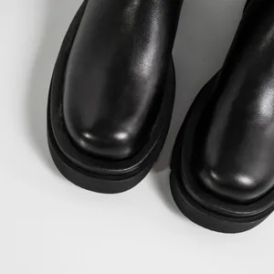 Primer plano de botas de cuero negro con punta redonda, textura premium y suela gruesa.