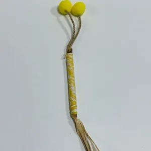 Detailed view of handmade cat silvervine molar stick with yellow pom-poms and raffia