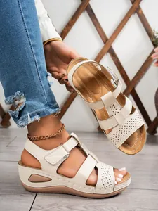 Detail view of stylish beige wedge sandals featuring laser-cut patterns and Velcro straps.