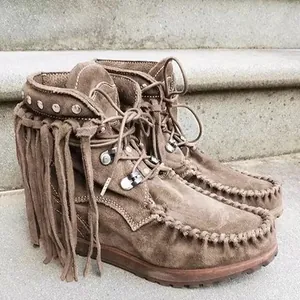 Detailed view of brown suede fringe boots with rivets and laces on stone steps.