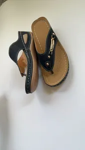 Vista detallada de sandalias de cuña negras con hebilla dorada y costuras blancas