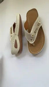Detalle de chanclas beige con cuña, perforaciones láser y cadena metálica dorada.