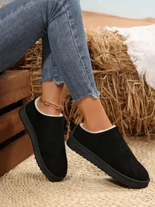 Detail view of black suede slip-on snow boots with warm faux fur lining on straw mat
