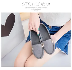 Detailed view of grey suede flat loafers with gold metal buckle held by an Asian model