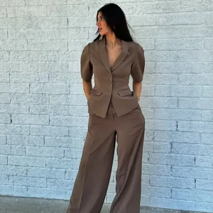 Élégant ensemble blazer marron à manches courtes et pantalon large devant un mur blanc