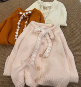 Dettaglio di cardigan in maglia con fiocco per bambini in rosa, crema e arancione