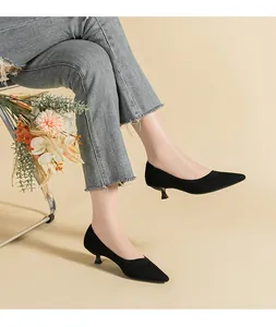 Macro view of black knitted pointed-toe kitten heels worn by model on beige background.
