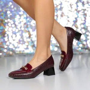 Dettaglio di décolleté bordeaux effetto coccodrillo con fibbia dorata e tacco largo