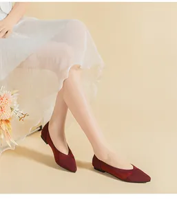 Detail shot of elegant burgundy woven pointed-toe flat shoes worn by a model in a white skirt
