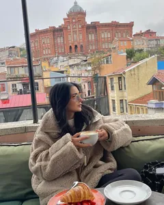 Frau trägt eine beige Plüsch-Fleecejacke in einem gemütlichen Outdoor-Café auf dem Dach.