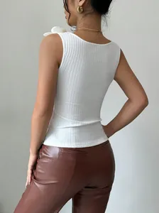 Dettaglio del top bianco a maglia con un'elegante decorazione floreale 3D sulla spalla.