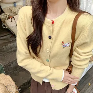 Detailed view of yellow knitted cardigan with colorful buttons and dog embroidery.