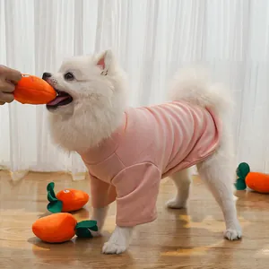 Detail shot of a small white dog playing with a plush carrot squeaky toy on a wooden floor