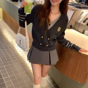 Junges Model trägt eine graue Strickjacke im Preppy-Stil und einen Faltenrock