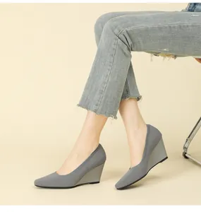 Close-up view of stylish grey square-toe knitted wedge heels worn with denim jeans.