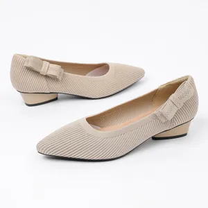 Detail view of beige knitted pointed toe pumps with a decorative bow on the heel