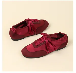 Detail view of burgundy satin and suede ballet flats with ribbon laces and soft soles.