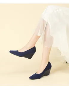 Elegant navy blue knit wedge pumps shown on a model's feet with a white skirt.