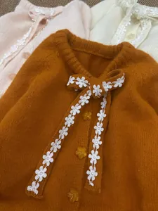 Dettaglio ravvicinato di cardigan in maglia con fiocco in pizzo floreale e bottoni a stella