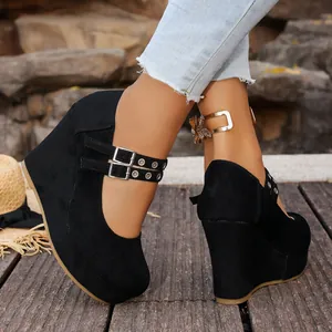 Primer plano de cuñas de ante negro con elegantes hebillas metálicas en un entorno exterior.