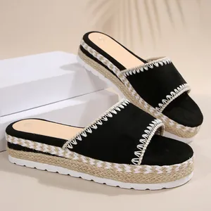 Detailweergave van zwarte sleehak-slippers met witte stiksels en plateauzool van jute