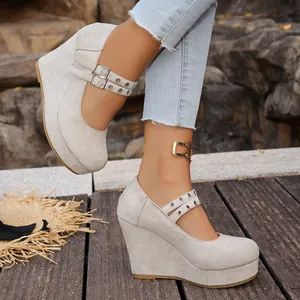 Detalle de zapatos de cuña beige con hebilla de corazón y plataforma sobre una terraza.
