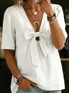 Détail d'une blouse blanche à col en V avec un nœud papillon devant et texture effet lin