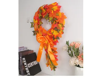 Artificial maple leaf harvest wreath with orange satin bow hanging on a white wall