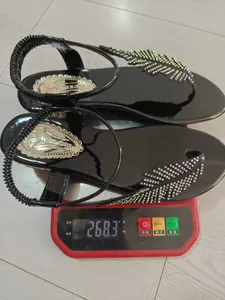 Vue détaillée de la mesure du poids de ces sandales noires à plumes et strass sur une balance