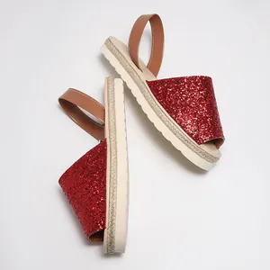 Close-up detail of sparkly red glitter sequins and brown leather straps on flat sandals