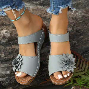 Close-up of stylish light grey wedge sandals with floral ornament on a wood background